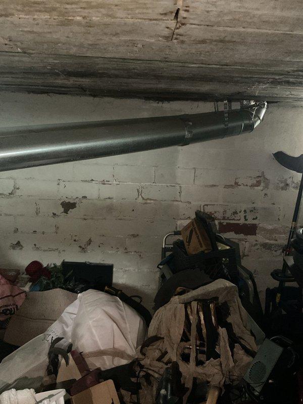 Performed inspection of existing furnace system in basement utility area. Unit shows signs of age and wear with deteriorating components. Evaluated ductwork condition, noting metal connections along concrete ceiling. Documented current installation against brick wall with copper piping and electrical connections. Provided replacement options for complete system upgrade based on assessment.