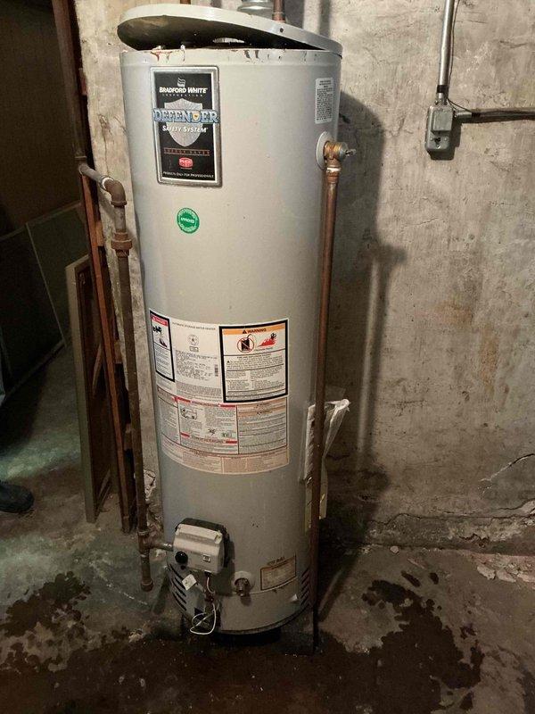 Diagnosed and repaired leaking Bradford White tanked water heater in 120-year-old residence. Identified water pooling at base of unit and moisture staining on concrete floor, indicating tank failure. Replaced aging water heater with proper connections to existing copper plumbing system.