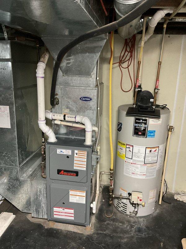 Conducted comprehensive site assessment for AC replacement quote, examining the existing outdoor unit (showing signs of weathering with rusted disconnect box) and the indoor HVAC system (Amana furnace with Carrier ductwork components). Evaluated current installation configuration including condensate drainage, electrical connections, and integration with the home's water heating system to determine optimal replacement specifications.