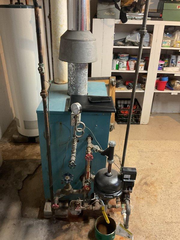 Performed comprehensive inspection of aging Atlas Heating Co. steam boiler system showing signs of corrosion and wear, particularly on the exhaust flue and connecting pipework. Documented current system configuration including water heater integration, pump/control unit, and valve assembly for replacement estimate. Recommended full system upgrade due to efficiency concerns and deteriorating components.