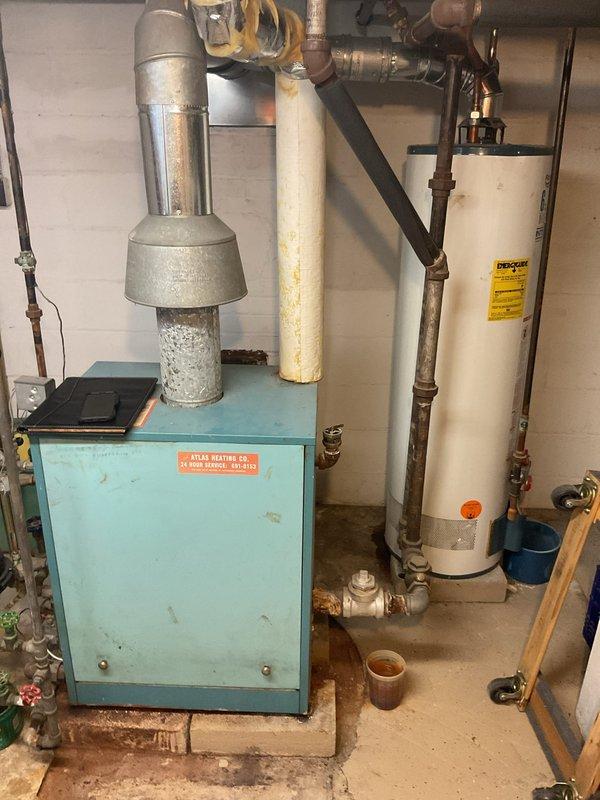 Performed comprehensive inspection of aging Atlas Heating Co. steam boiler system showing signs of corrosion and wear, particularly on the exhaust flue and connecting pipework. Documented current system configuration including water heater integration, pump/control unit, and valve assembly for replacement estimate. Recommended full system upgrade due to efficiency concerns and deteriorating components.