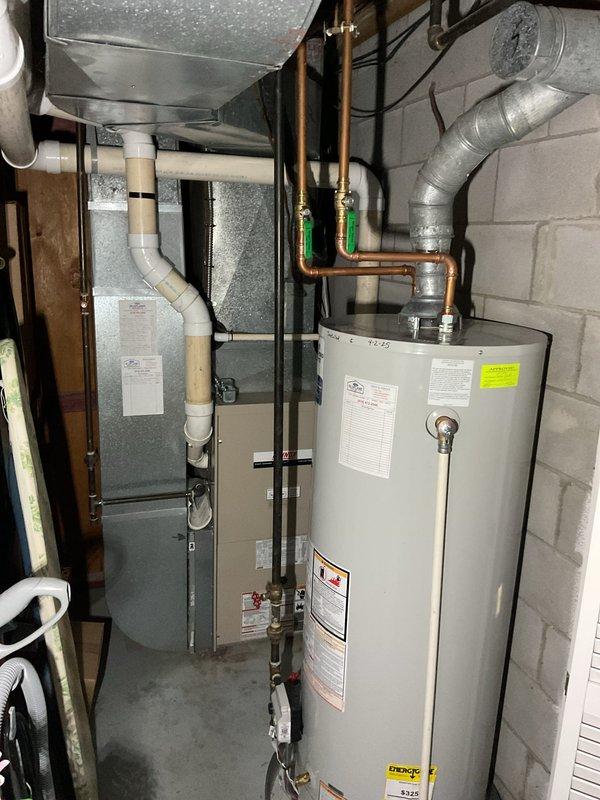 Performed comprehensive assessment of existing residential HVAC system and water heater installation in utility room. System features properly installed cylindrical water heater with copper piping connections, functioning valves, and associated PVC drainage components. Evaluation included inspection of the air handler unit, ductwork condition, and all mechanical connections to determine appropriate replacement options.