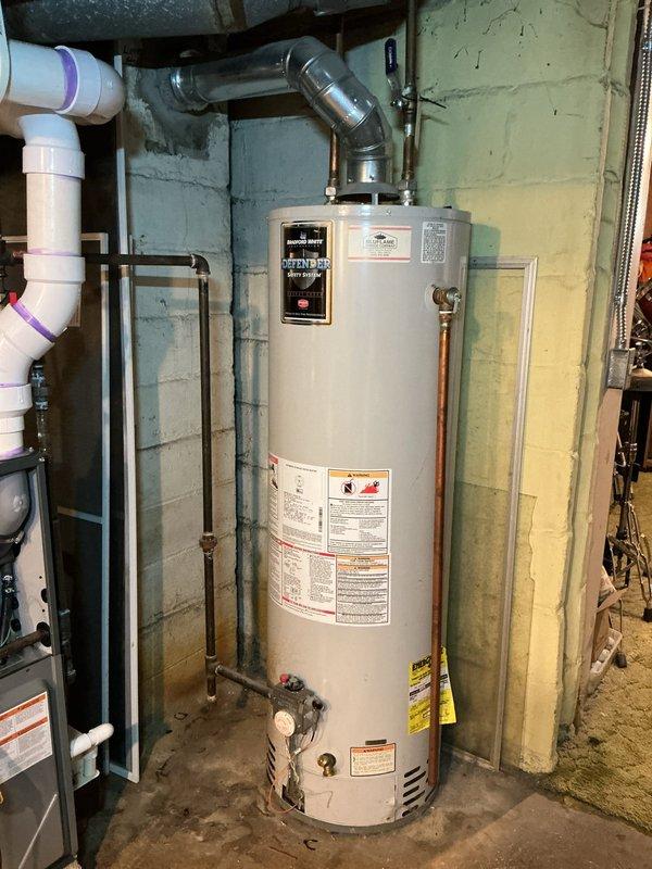 Completed Amana warranty replacement by installing new Bradford White Defender water heater system in utility room. Installation included proper connection of copper supply/return lines, metal vent piping with 90-degree elbow, and verification of all safety systems. BluFlame service label applied and unit tested for proper operation.