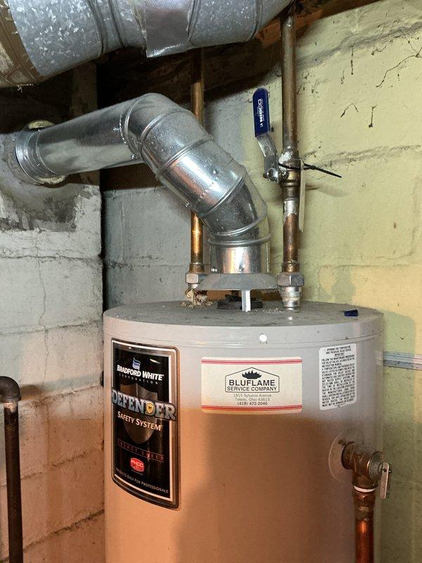 Completed Amana warranty replacement by installing new Bradford White Defender water heater system in utility room. Installation included proper connection of copper supply/return lines, metal vent piping with 90-degree elbow, and verification of all safety systems. BluFlame service label applied and unit tested for proper operation.