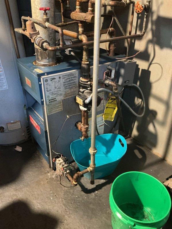 Responded to service call for 10-year-old boiler with active water leak. Upon inspection, identified severe corrosion and mineral buildup on copper piping at T-junction connection, particularly evident at connection points. Placed collection buckets under affected area to prevent water damage to customer's property while repairs were completed.