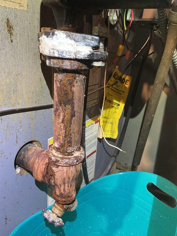 Responded to service call for 10-year-old boiler with active water leak. Upon inspection, identified severe corrosion and mineral buildup on copper piping at T-junction connection, particularly evident at connection points. Placed collection buckets under affected area to prevent water damage to customer's property while repairs were completed.