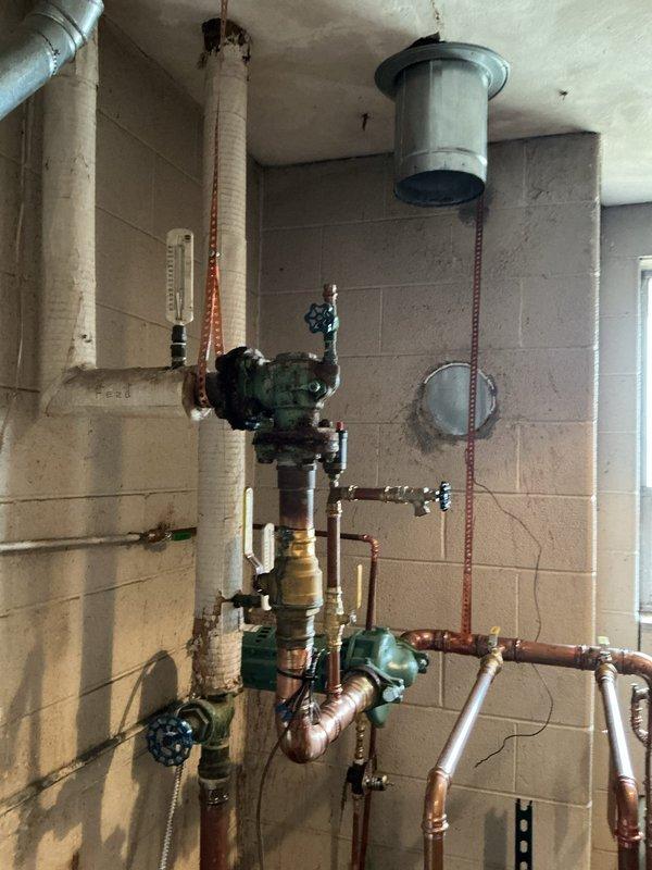Performed diagnostic assessment on 10+ year old boiler system that was non-operational. Inspected complex piping arrangement including pressure regulator, multiple valves, and copper distribution lines. Identified oxidation on central valve assembly and signs of water damage on surrounding concrete block wall; recommended system replacement due to age and deterioration of critical components.