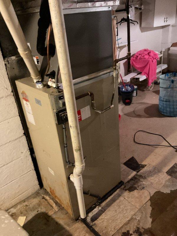 Inspected non-operational furnace of indeterminate age located in basement utility area. Visual examination revealed an aging beige/tan unit installed against cinder block wall with visible moisture staining around base. Recommended complete system replacement due to age-related component failure and signs of water damage that could impact reliable operation.