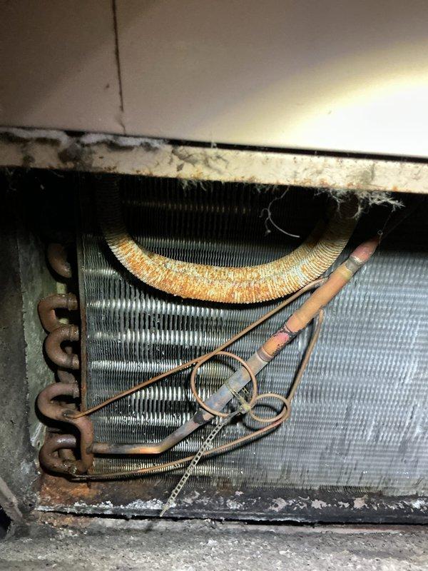 Responded to service call for leaking and frozen furnace coils. Inspection revealed significant dust accumulation, possible corrosion, and deterioration on evaporator coil assembly with orange discoloration on upper portions. Observed copper refrigerant lines with compromised insulation and evidence of moisture issues causing freezing.