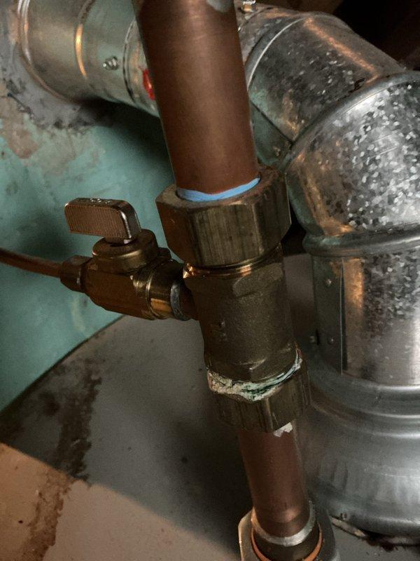 Conducted water heater installation estimate in utility area, documenting existing copper piping with brass shutoff valve showing signs of age and mineral buildup. Noted significant wall damage around pipe penetration point with crumbling material and extensive cracking, indicating possible previous water damage that will need to be addressed during installation.