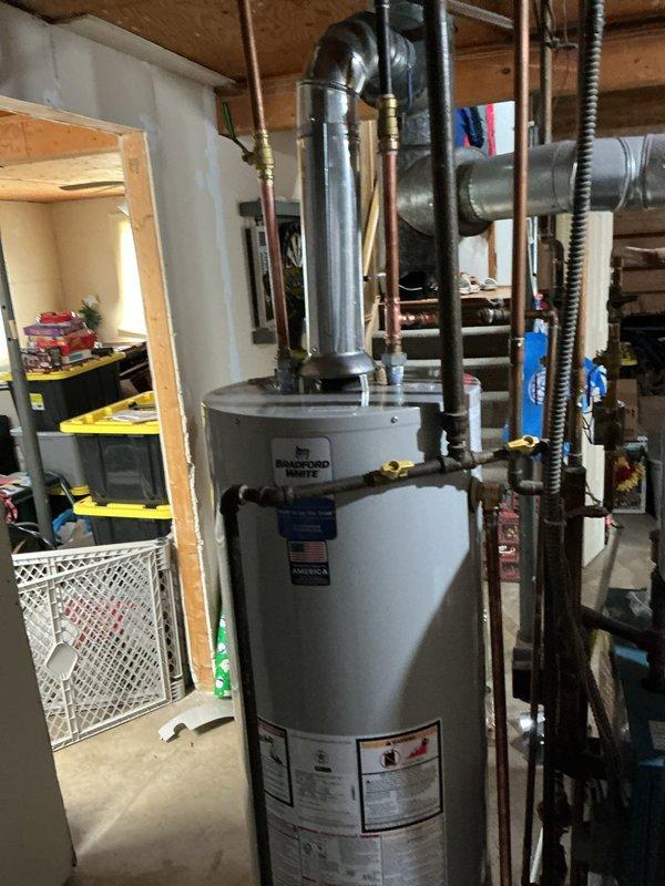 Responded to service call for reported tankless water heater malfunction at residential property. Upon arrival, found A.O. Smith ProMax conventional tank-style water heater installed in basement utility room, not a tankless unit as initially reported. Performed diagnostic inspection of water heater and associated plumbing connections, including copper supply lines, shut-off valves, and venting system. Verified proper installation configuration with metallic ductwork and exhaust venting. Unit appeared operational with all safety labels and manufacturer specifications visible and intact. Documented existing installation with photographs showing water heater positioning, piping connections, and mechanical room layout for service records.