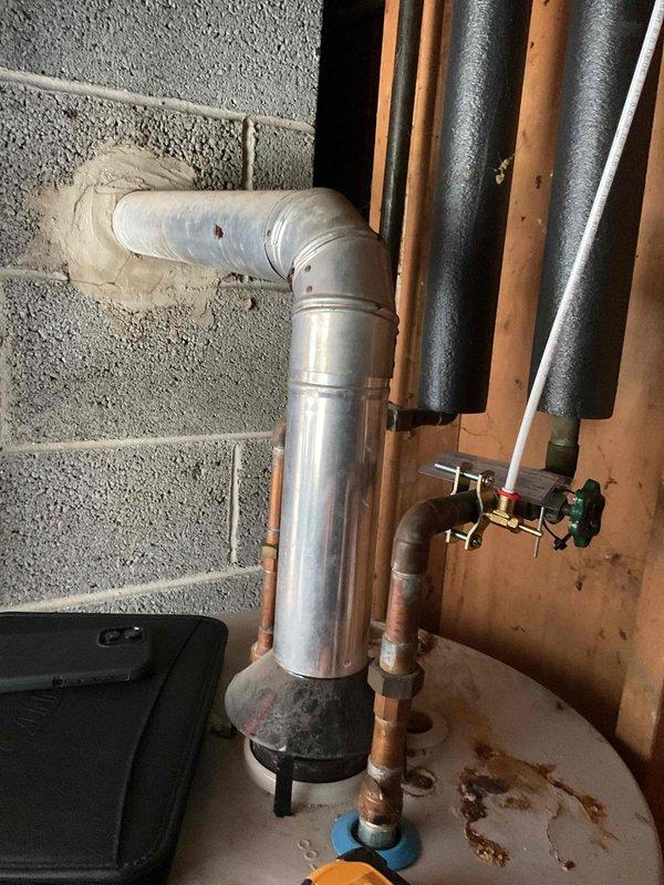 Conducted comprehensive water heater replacement estimate at residential property. Assessed existing water heater installation including galvanized steel flue vent system with vertical run and elbow configuration, copper supply and distribution piping with brass shut-off valves, and current mounting platform. Documented plumbing connections, venting arrangement, clearances to combustible materials, and proximity to concrete block foundation wall. Photographed existing installation showing foam pipe insulation on hot water lines, galvanized vent pipe condition with visible wear, and copper piping with aged patina. Evaluated accessibility for equipment removal and replacement within unfinished utility space with exposed wall studs. Noted existing valve locations, pipe sizing, and connection points for new unit installation. Provided detailed assessment for complete water heater replacement including removal of existing unit, installation of new water heater with proper venting, connectio