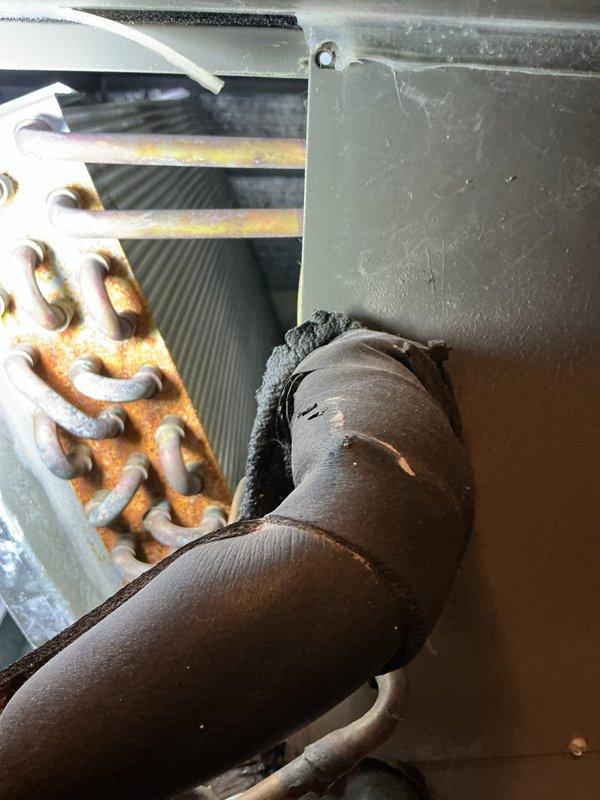 Completed comprehensive preventive maintenance tune-up on an 18-year-old Lennox air conditioning system located at rear of property. Performed full system inspection including visual assessment of indoor air handler components, refrigerant lines, condensate drainage system, and heat exchanger coils. Noted significant rust and corrosion present on copper refrigerant coil components, which is consistent with the age of the equipment. Verified proper insulation on refrigerant lines, checked condensate drain functionality with white PVC piping configuration, and documented system condition with diagnostic equipment. All accessible components were inspected and system operational status confirmed.