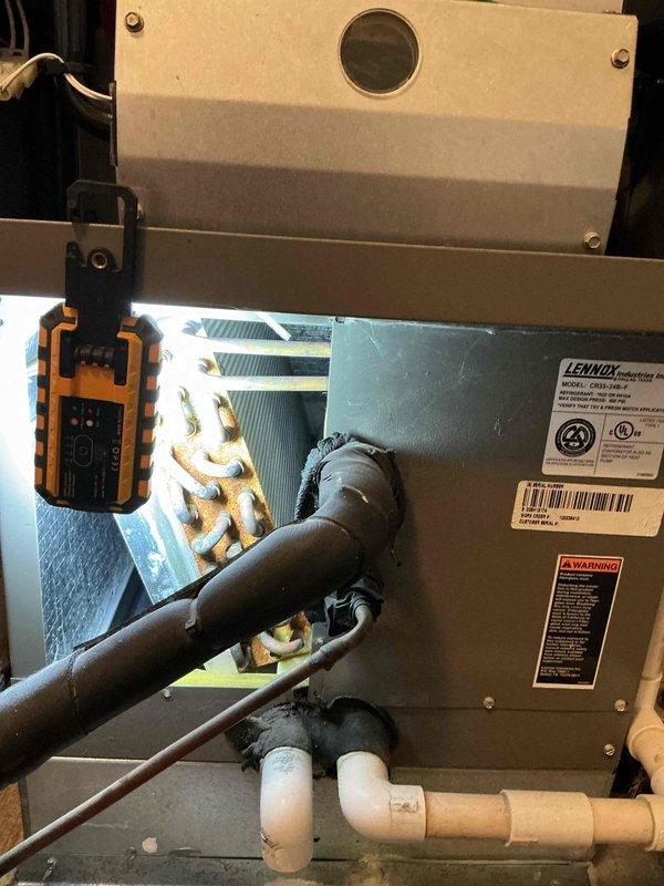 Completed comprehensive preventive maintenance tune-up on an 18-year-old Lennox air conditioning system located at rear of property. Performed full system inspection including visual assessment of indoor air handler components, refrigerant lines, condensate drainage system, and heat exchanger coils. Noted significant rust and corrosion present on copper refrigerant coil components, which is consistent with the age of the equipment. Verified proper insulation on refrigerant lines, checked condensate drain functionality with white PVC piping configuration, and documented system condition with diagnostic equipment. All accessible components were inspected and system operational status confirmed.