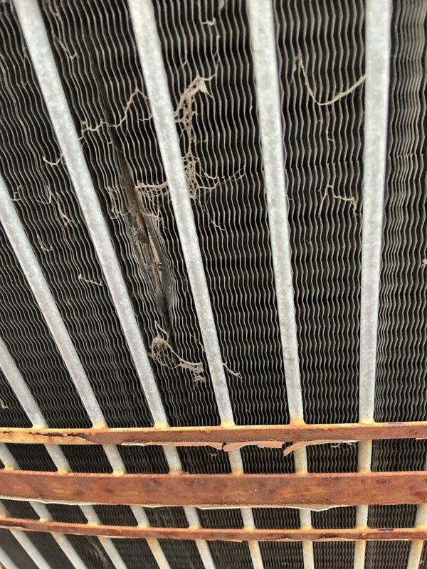 Performed scheduled air conditioning maintenance on unknown age system. Upon inspection, found evaporator coil fins with moderate to heavy dust and debris accumulation affecting airflow efficiency. Noted physical damage to upper section of coil assembly with bent and torn fins requiring attention. Documented condition of heat exchanger components showing signs of extended service life, including weathered copper support grid with patina buildup and white residue coating on fin surfaces. Completed standard maintenance procedures and provided photographic documentation of system condition for customer records.