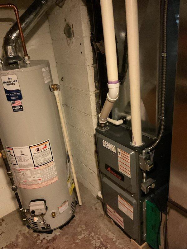 Completed comprehensive air conditioning system estimate for residential HVAC replacement. Evaluated existing outdoor condensing unit with tan cylindrical casing positioned on concrete pad alongside building exterior, noting current equipment specifications and installation configuration including electrical disconnect and conduit routing. Assessed indoor basement equipment including existing furnace unit with PVC venting system installed adjacent to water heater in mechanical room. Documented current system layout, equipment age and condition, electrical connections, refrigerant line routing, and ductwork configuration. Provided detailed replacement options and recommendations for complete HVAC system upgrade to improve efficiency and reliability.