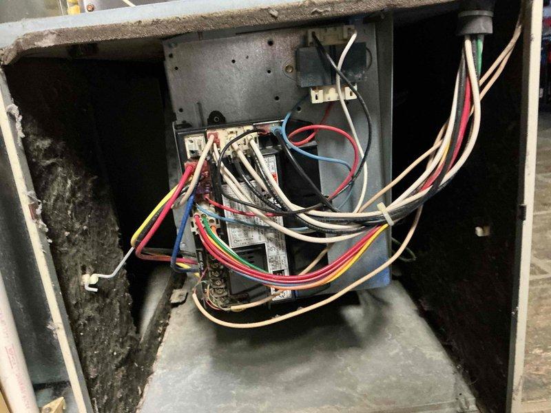 Responded to service call for residential air conditioning system with no cooling condition. Upon arrival, performed visual inspection of 20-year-old AC unit exterior components. Accessed electrical disconnect box mounted on building exterior and documented condition of disconnect switch and internal wiring. Opened control panel enclosure to inspect electrical connections, control board, and associated wiring harness. Found multiple wire connections to central control module with signs of age-related wear and deterioration. Noted disorganized wiring configuration and evidence of dust accumulation throughout electrical compartments. Photographed disconnect box components, warning labels, and internal control panel wiring for documentation purposes. Given the advanced age of the system and observed condition of electrical components, provided customer with assessment of unit status and discussed available options for repair versus replacement considerations.