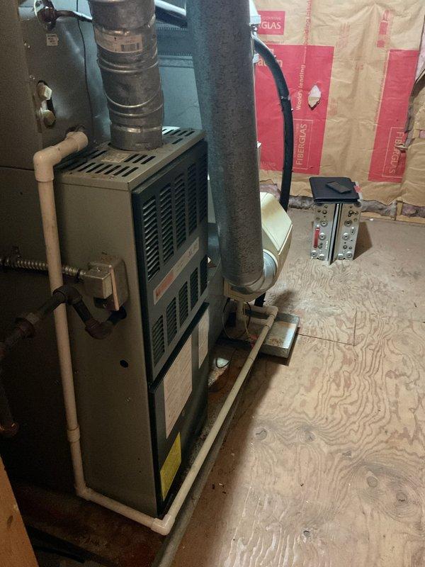 Conducted comprehensive site assessment for complete HVAC system replacement in unfinished basement mechanical space. Evaluated existing furnace/air handler unit and ductwork configuration for full system changeout. Documented current equipment specifications, including metal air handler with existing cylindrical ductwork wrapped in gray insulation material and beige metal supply plenum. Assessed installation area conditions, noting exposed OSB subflooring, partially finished walls with fiberglass insulation, and available clearances for new equipment placement. Photographed existing system components, duct connections, and spatial layout to develop accurate replacement proposal. Evaluated electrical service panel location and existing PVC condensate drainage routing for compatibility with new system installation requirements.