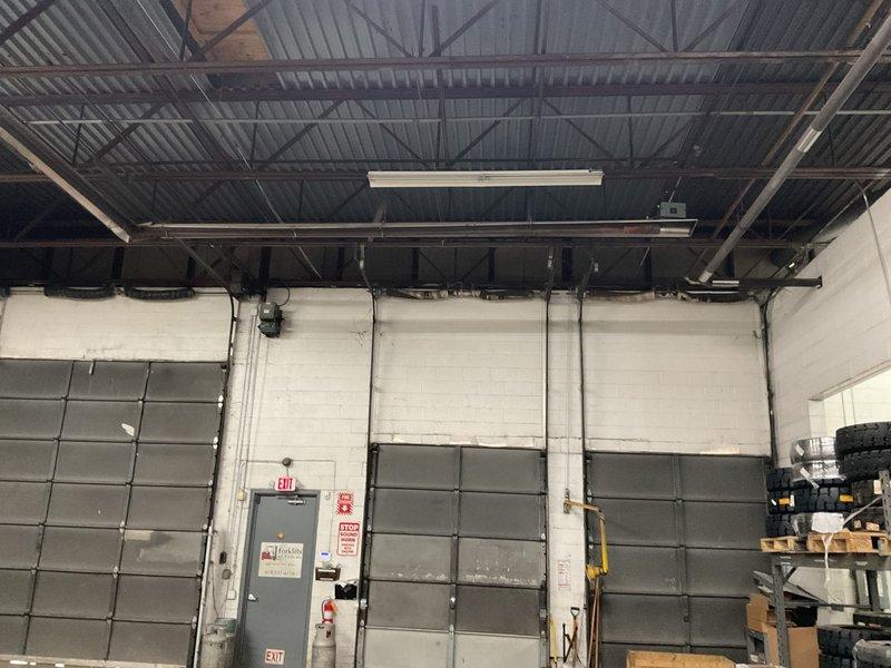 Completed site evaluation for industrial radiant tube heating system replacement in commercial warehouse facility. Assessed existing space configuration with exposed corrugated metal ceiling, structural truss framework, and overhead sectional doors. Documented field measurements for two-zone radiant tube heater layout: primary zone measuring 60 feet in length with 14.5-foot ceiling clearance, secondary zone at 120 feet, with 25-foot spacing intervals between units and 45-foot run specifications. Photographed current warehouse conditions including existing wall-mounted heating units, electrical infrastructure, and storage area clearances to ensure proper equipment placement and code compliance for proposed radiant tube heating system installation.