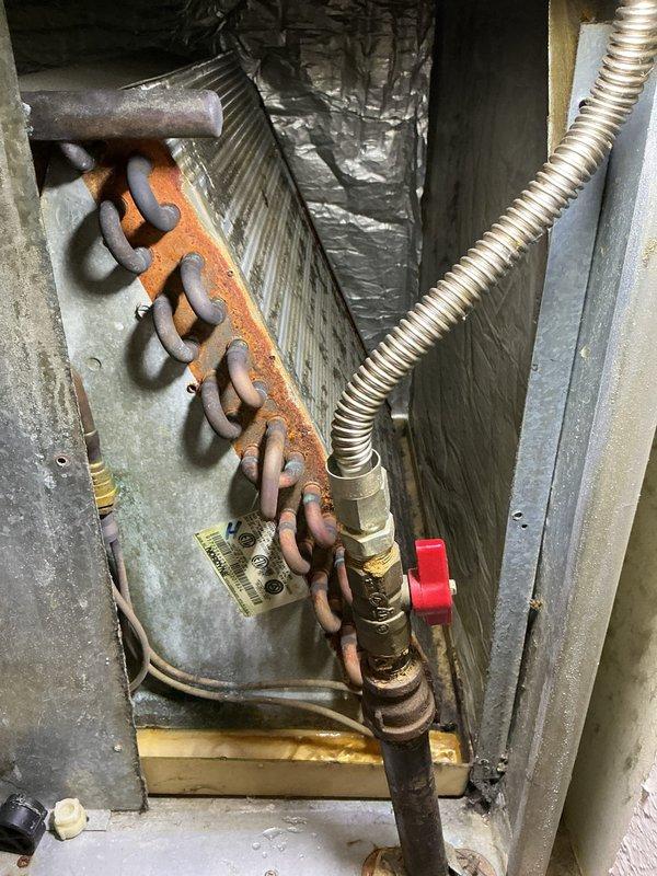 Responded to cooling maintenance call for 25-year-old HVAC system with locked access panel. Brought bolt cutters to remove lock per customer request due to lost key. Upon gaining access, performed system inspection and documented equipment condition with photos. Noted significant rust and corrosion on copper heating elements, heat exchanger coil assembly, and mounting hardware throughout the unit, consistent with age and moisture exposure. Inspected flexible metal conduit, brass valve fittings with red handle, evaporator coil with triangular fin patterns, and associated refrigerant line connections. All components showing operational wear and oxidation typical of 25-year service life. System operational following access restoration and inspection completion.