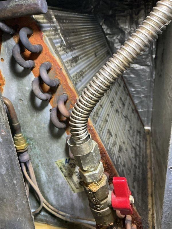 Responded to cooling maintenance call for 25-year-old HVAC system with locked access panel. Brought bolt cutters to remove lock per customer request due to lost key. Upon gaining access, performed system inspection and documented equipment condition with photos. Noted significant rust and corrosion on copper heating elements, heat exchanger coil assembly, and mounting hardware throughout the unit, consistent with age and moisture exposure. Inspected flexible metal conduit, brass valve fittings with red handle, evaporator coil with triangular fin patterns, and associated refrigerant line connections. All components showing operational wear and oxidation typical of 25-year service life. System operational following access restoration and inspection completion.