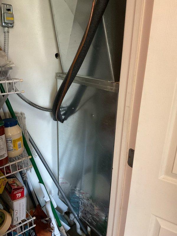 Completed comprehensive estimate for full air handler replacement in interior utility closet. Inspected existing gray metal air handler unit showing visible moisture damage, water streaking, and surface discoloration indicating potential condensate drainage issues or cabinet deterioration. Evaluated refrigerant line configuration with copper piping and insulation routing, electrical connections via flexible metallic conduit, and overall system accessibility within confined space alongside existing storage shelving. Assessed outdoor condensing unit positioned on rooftop concrete pad adjacent to brick wall, noting weathered exterior surfaces and age-related wear patterns. Provided detailed replacement recommendations including proper equipment sizing, condensate management solutions, and installation specifications for new air handler system to address moisture concerns and restore reliable indoor climate control.