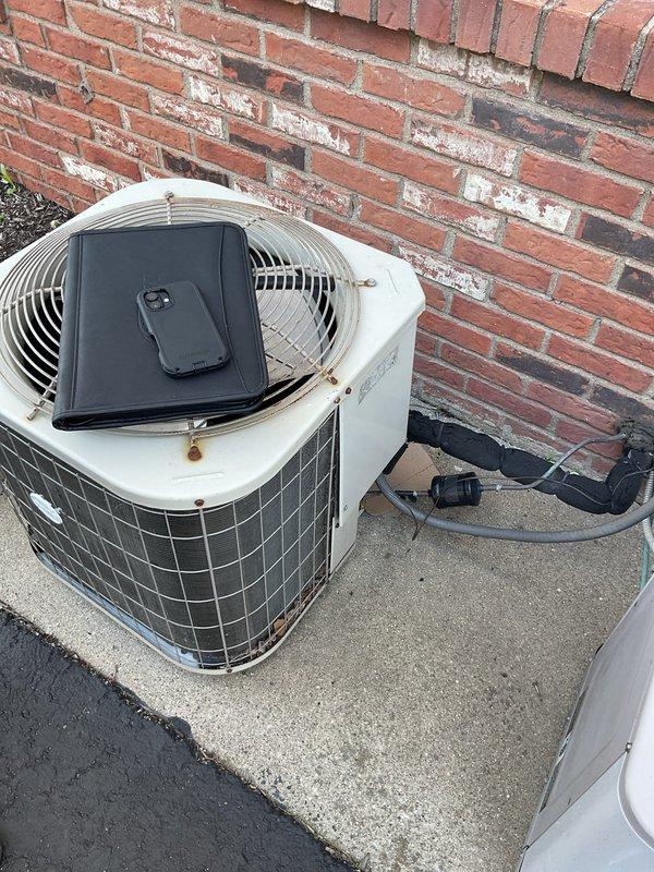 Completed comprehensive estimate for full air handler replacement in interior utility closet. Inspected existing gray metal air handler unit showing visible moisture damage, water streaking, and surface discoloration indicating potential condensate drainage issues or cabinet deterioration. Evaluated refrigerant line configuration with copper piping and insulation routing, electrical connections via flexible metallic conduit, and overall system accessibility within confined space alongside existing storage shelving. Assessed outdoor condensing unit positioned on rooftop concrete pad adjacent to brick wall, noting weathered exterior surfaces and age-related wear patterns. Provided detailed replacement recommendations including proper equipment sizing, condensate management solutions, and installation specifications for new air handler system to address moisture concerns and restore reliable indoor climate control.
