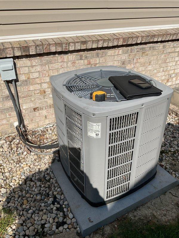 Conducted comprehensive evaluation of existing HVAC system including outdoor condensing unit and indoor furnace for potential replacement. Assessed current gray cylindrical air conditioning unit positioned on concrete pad with river rock landscaping, noting refrigerant line set routing and electrical connections to structure. Evaluated basement furnace installation including existing ductwork configuration, PVC venting system, and overall equipment condition. Documented equipment specifications, measured system components, and photographed installation details to provide accurate replacement options for complete HVAC system upgrade.