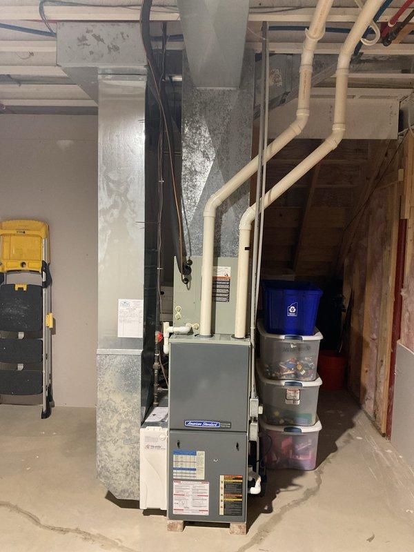 Conducted comprehensive evaluation of existing HVAC system including outdoor condensing unit and indoor furnace for potential replacement. Assessed current gray cylindrical air conditioning unit positioned on concrete pad with river rock landscaping, noting refrigerant line set routing and electrical connections to structure. Evaluated basement furnace installation including existing ductwork configuration, PVC venting system, and overall equipment condition. Documented equipment specifications, measured system components, and photographed installation details to provide accurate replacement options for complete HVAC system upgrade.