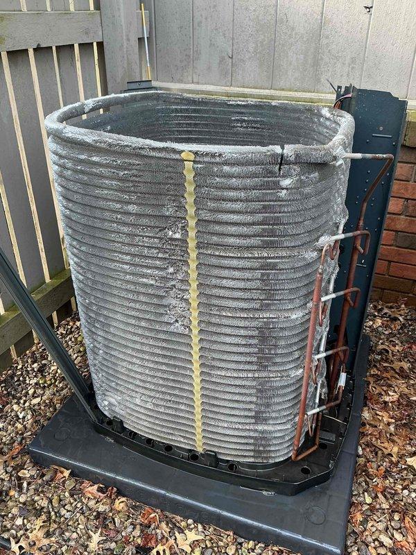 Completed second appointment to troubleshoot HVAC system with problematic dampers previously identified during initial diagnostic visit. Performed comprehensive A/C tune-up on outdoor condensing unit, including inspection of cylindrical coil assembly which showed weathering, mineral deposits, and debris accumulation between fins. Documented unit condition with exterior coil displaying surface discoloration and foam insulation material along refrigerant line connections, with system mounted on rubber pad in gravel bed adjacent to property fence line.