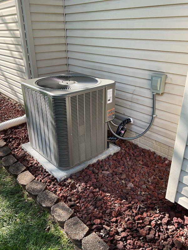Completed full HVAC system installation including a 14 SEER 3.5-ton air conditioning condensing unit with matching evaporator coil. Installed new 7/8" x 50' refrigerant line set connecting the outdoor condensing unit to the indoor coil mounted on the existing Concord furnace. Positioned condensing unit on new concrete pad against exterior wall with decorative rock landscaping for proper drainage and clearance. Installed new electrical disconnect box and whip for code-compliant power supply to the condensing unit. Mounted L-40 thermostat to control the new cooling system. All refrigerant lines were properly insulated and secured. Electrical connections were completed per manufacturer specifications and local code requirements. System was pressure tested for leaks, evacuated, and charged with appropriate refrigerant to manufacturer specifications. Verified proper airflow, temperature differential, and system operation. All components functioning as designed with proper drainage establish
