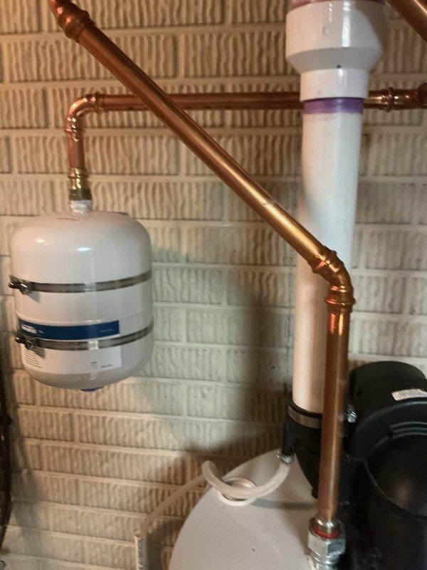 Responded to service call for leaking tanked water heater that was recently installed by another contractor and still under warranty period. Upon inspection, identified leak source in the plumbing connections associated with the water heater system. The installation included an expansion tank, copper piping with multiple bends and connections, circulation pump components, and backflow prevention devices mounted on the brick wall. Documented the existing installation configuration with photographs showing the expansion tank, copper pipe routing, soldered joints, and associated plumbing components for warranty claim purposes. Verified proper installation of expansion tank with metal mounting straps and assessed the overall system layout including the PVC connections and circulation equipment. Recommended contacting the original installing contractor to address the leak under the existing warranty coverage.