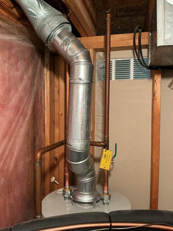 Conducted on-site assessment of existing water heater system in basement utility area for replacement estimate. Evaluated current gas-fired water heater installation, including connections to gas supply line with yellow T-handle shut-off valve, existing copper plumbing connections, and galvanized metal venting system with flexible duct transition. Documented configuration of surrounding mechanical systems including proximity to HVAC equipment and available workspace for replacement unit. Photographed current installation showing water heater positioning, venting arrangement through wooden framing, copper supply lines with brass fittings, and basement infrastructure to provide accurate replacement specifications and installation requirements.