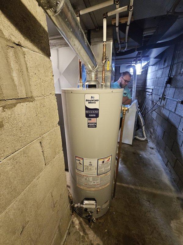 Completed installation of a 50-gallon Bradford White tanked water heater in basement utility area. Unit was properly positioned on concrete floor with all copper supply lines, fittings, and safety valves connected according to manufacturer specifications and local plumbing codes. All connections were tested and verified operational.