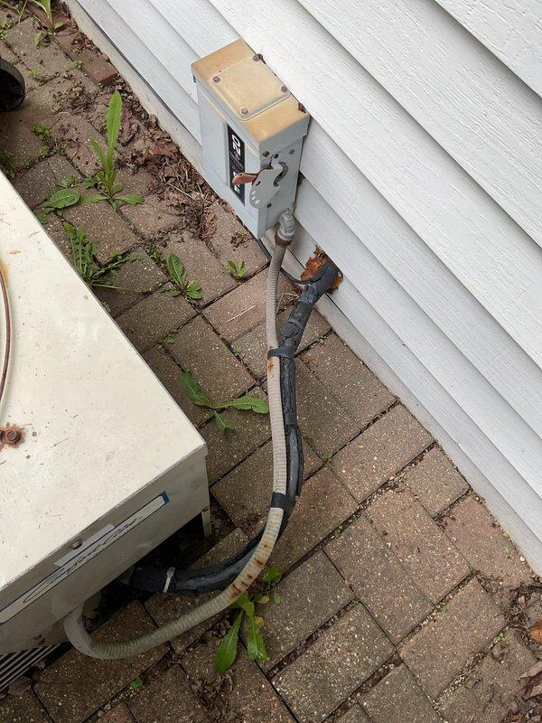 Conducted comprehensive site evaluation of existing outdoor air conditioning condenser unit for replacement estimate. Unit exhibited visible aging, wear, and discoloration consistent with extended service life. Documented current installation configuration including electrical disconnect box, conduit routing, refrigerant line sets with insulation sleeves, and equipment positioning on brick paver base. Assessed existing infrastructure conditions and photographed equipment specifications to determine appropriate replacement system requirements and installation parameters.