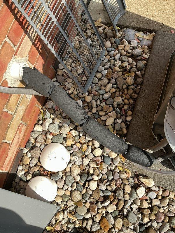 Performed routine cooling maintenance on a 5-year-old air conditioning system. Inspected outdoor disconnect box and fuse assembly, confirming proper electrical connections and fuse integrity. Examined rooftop condensing unit installation, verified secure mounting, checked refrigerant lines and electrical conduit routing through decorative rock ballast area. All components found in good working condition with normal wear for unit age.