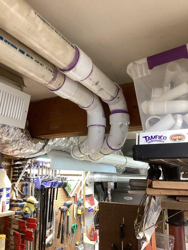 Responded to warranty callback for new HVAC installation with water leaking from exhaust condensate line along ceiling in garage workspace. Upon inspection, identified improper drainage slope in white PVC condensate piping system running across ceiling joists. Condensate line showed purple primer markings at joints but exhibited insufficient pitch toward drain termination point, causing water to pool and leak at fitting connections. Verified flexible ductwork and air handler unit mounted nearby showed no signs of moisture damage. Adjusted and re-secured PVC piping with proper downward slope using appropriate hangers and straps to ensure gravity drainage. Tested system operation and confirmed condensate flowing properly through drain line without backup or leakage. Installation now meets code requirements for proper condensate removal.