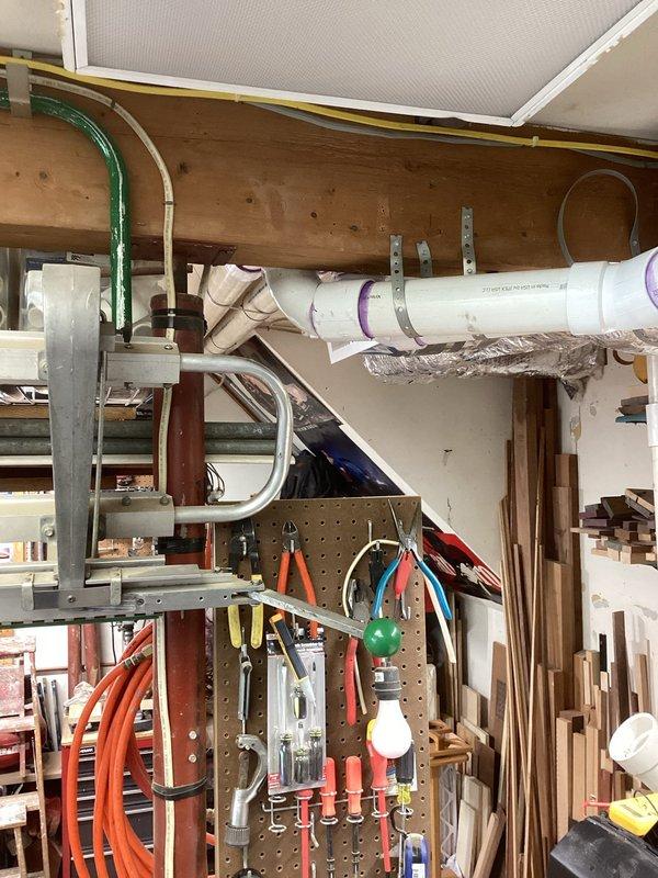 Responded to warranty callback for new HVAC installation with water leaking from exhaust condensate line along ceiling in garage workspace. Upon inspection, identified improper drainage slope in white PVC condensate piping system running across ceiling joists. Condensate line showed purple primer markings at joints but exhibited insufficient pitch toward drain termination point, causing water to pool and leak at fitting connections. Verified flexible ductwork and air handler unit mounted nearby showed no signs of moisture damage. Adjusted and re-secured PVC piping with proper downward slope using appropriate hangers and straps to ensure gravity drainage. Tested system operation and confirmed condensate flowing properly through drain line without backup or leakage. Installation now meets code requirements for proper condensate removal.