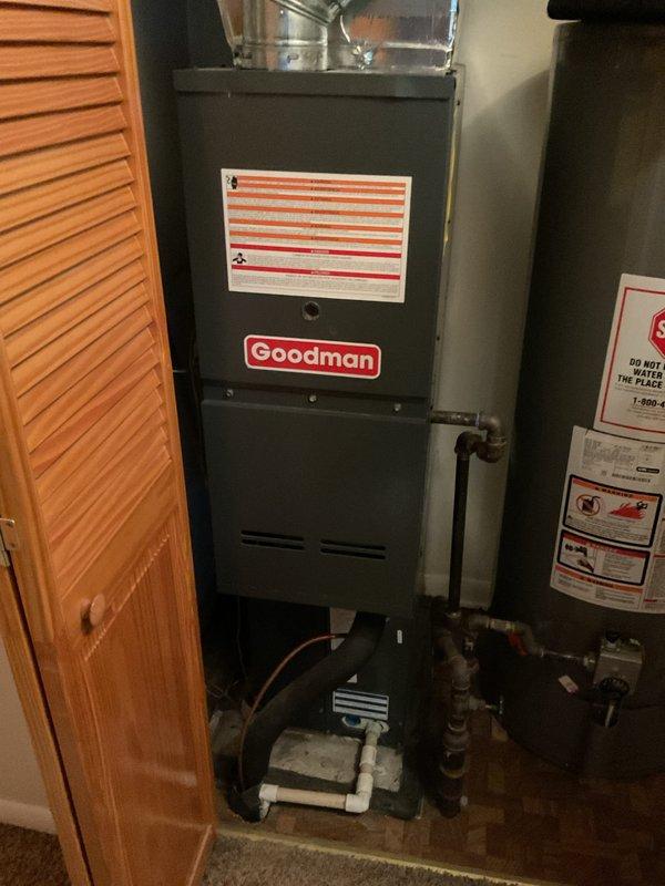 Conducted on-site evaluation of existing Goodman furnace installation in residential utility closet to provide replacement estimate. Customer initially requested air conditioning system estimate but expressed interest in complete HVAC system replacement. Documented current equipment configuration including furnace unit, ductwork connections, condensate pump assembly, and adjacent water heater. Photographed existing installation showing metallic supply plenum, insulated ductwork with visible wear and discoloration, gas line connections, and confined installation space with louvered access door. Assessed equipment condition, spatial constraints, and utility connections to prepare comprehensive replacement options for both standalone AC unit and full heating/cooling system upgrade.