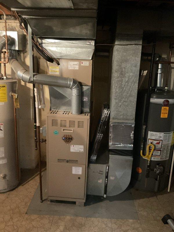 Conducted comprehensive assessment of existing HVAC system in residential basement mechanical room for furnace replacement estimate. Evaluated current beige-colored furnace unit including condition of ventilation components, ductwork connections, and overall system configuration. Documented existing equipment layout with two water heaters present in mechanical room, noting spatial considerations and clearance requirements for replacement unit installation. Assessed silver metal ductwork routing from furnace including flexible duct connections to determine compatibility with new equipment specifications. Photographed electrical panel locations and utility infrastructure on concrete block walls to identify power supply considerations for replacement furnace. Evaluated floor space and protective platform requirements for new unit placement. Obtained customer billing address information as requested to complete estimate documentation.