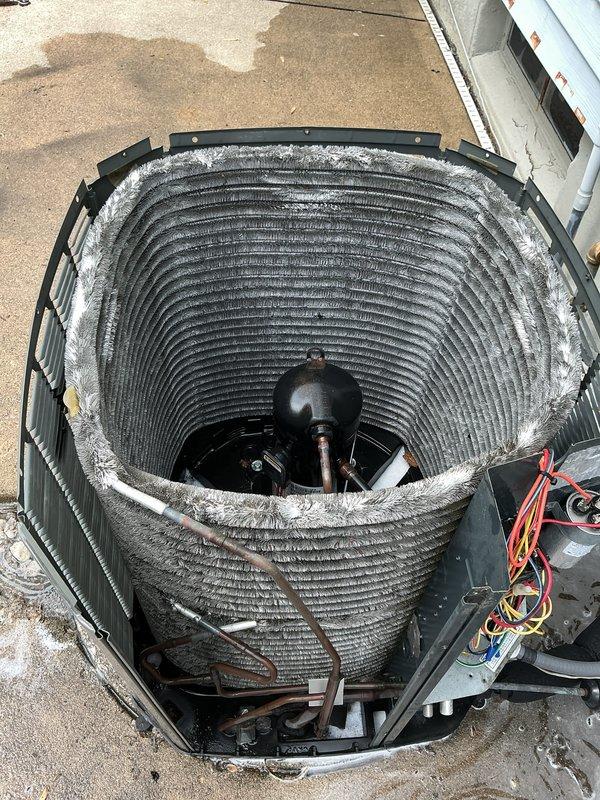 Completed annual cooling maintenance on a 5-year-old residential air conditioning system. Removed top panel to access condenser coil assembly, which exhibited significant accumulation of dust, lint, and debris throughout the barrel-style coil fins and grooves. Thoroughly cleaned condenser coil to restore proper airflow and heat transfer efficiency. Inspected electrical components including contactor, capacitor, and all wire connections, verifying secure terminations and proper operation. System tested and confirmed operational following maintenance procedures.