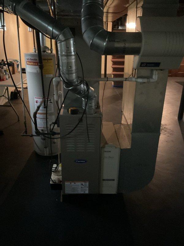 Completed comprehensive AC estimate for full HVAC system replacement in residential basement installation. Evaluated existing Carrier furnace unit, ductwork configuration, and overall heating and cooling infrastructure to provide replacement recommendations. Documented current system layout including vertical furnace positioning, black ductwork distribution across ceiling joists, and integration with existing water heater placement for proper spacing and clearance requirements in utility area.