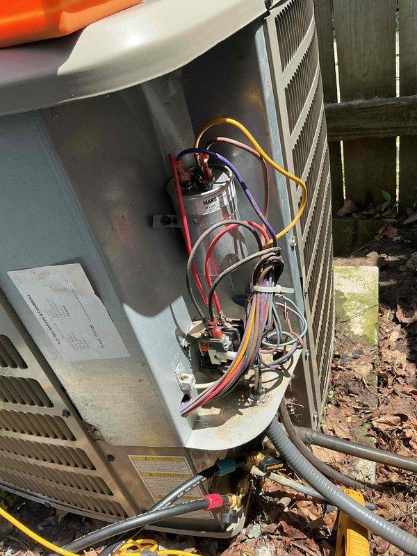 # HVAC Service Report

Responded to no cooling complaint on 4-year-old residential air conditioning system. Upon arrival, accessed electrical compartment and inspected internal components including dual run capacitor, contactor, and associated wiring connections. Verified all electrical connections were secure with proper wire routing observed on red, yellow, purple, and white conductor leads. Evaluated outdoor condensing unit positioned against perimeter fence, noting unit sitting on concrete pad with adequate clearance. Confirmed condenser coil fins intact and fan assembly operational with proper hub configuration. System restored to normal cooling operation following diagnostic evaluation and component verification.