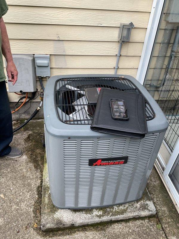 Completed equipment estimate for HVAC system replacement including indoor Amana furnace unit installed in basement utility area and outdoor air conditioning condenser unit positioned on concrete pad against exterior wall. Installation includes proper PVC drainage and ventilation piping, insulated refrigerant lines, metal ductwork integration, electrical disconnect box, and all necessary connections for complete heating and cooling system operation.
