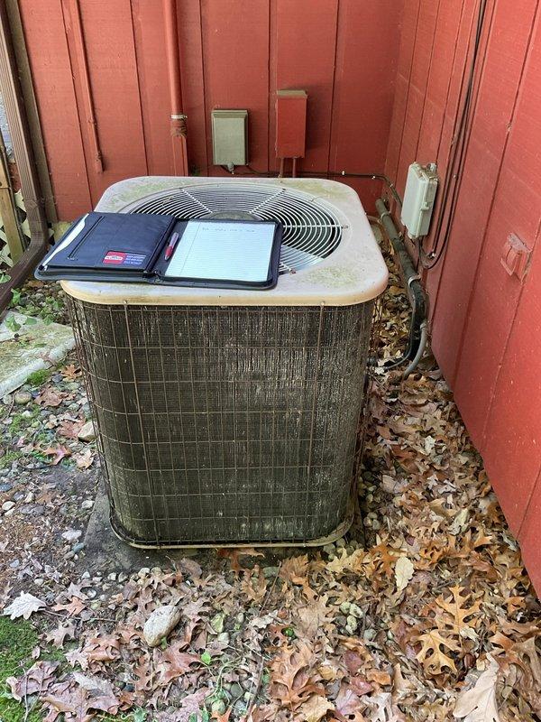 Conducted comprehensive site evaluation of existing outdoor air conditioning condenser unit for replacement estimate. Unit exhibited significant age-related deterioration with heavy dirt and grime accumulation on exterior grille surfaces and casing. Documented current system configuration including copper refrigerant line routing, electrical conduit connections, and junction box placement on building exterior. Assessed installation area conditions including concrete pad integrity, clearance requirements, and accessibility for replacement equipment. Photographed existing unit positioning against building structure and utility connections to ensure proper sizing and placement specifications for new system installation.