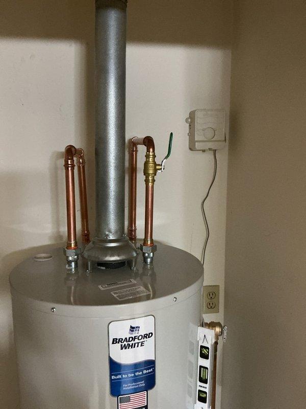 Completed professional installation of a Bradford White residential tanked water heater in utility room. Connected hot and cold water supply lines using copper piping with proper shut-off valves and dielectric unions. Installed metallic exhaust flue venting system extending vertically from unit top for safe combustion gas discharge. Verified level installation of unit to ensure proper operation and sediment settling. All plumbing connections soldered and pressure tested for leaks. Electrical components and wall-mounted controls properly wired and secured. Installation meets manufacturer specifications and local building codes for professional water heater replacement.
