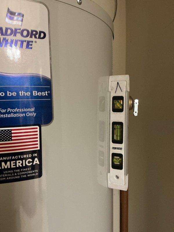 Completed professional installation of a Bradford White residential tanked water heater in utility room. Connected hot and cold water supply lines using copper piping with proper shut-off valves and dielectric unions. Installed metallic exhaust flue venting system extending vertically from unit top for safe combustion gas discharge. Verified level installation of unit to ensure proper operation and sediment settling. All plumbing connections soldered and pressure tested for leaks. Electrical components and wall-mounted controls properly wired and secured. Installation meets manufacturer specifications and local building codes for professional water heater replacement.