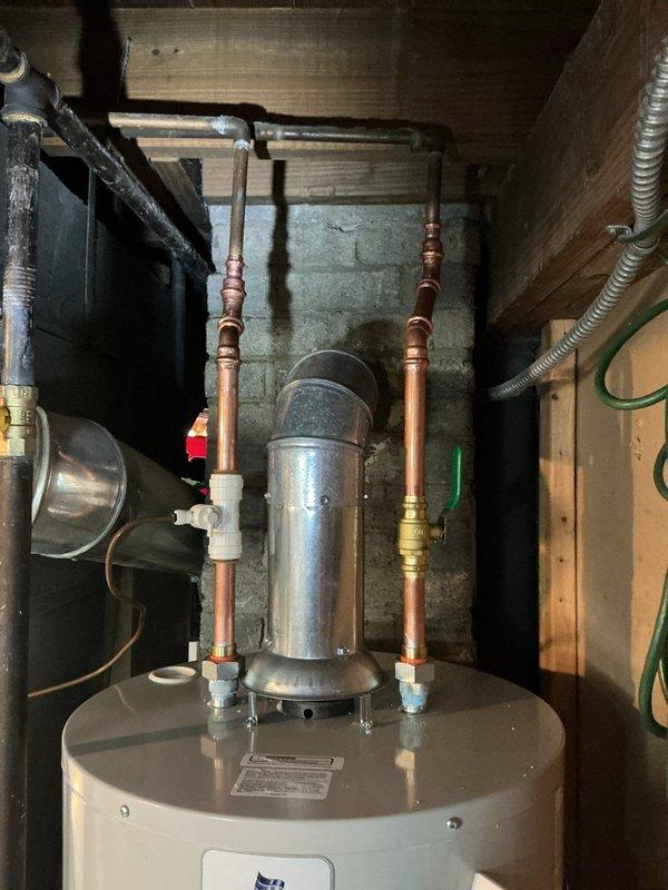 Completed residential water heater replacement in utility room. Removed existing unit and installed new white cylindrical water heater with proper safety labeling and operational specifications. Connected copper supply lines with shut-off valves (red and green handles) to top of unit, installed expansion tank, and secured all brass fittings and connections. Installed gas control valve with indicator light at base of unit, connected flexible gas line, and verified all electrical wiring connections. All plumbing connections tested and confirmed leak-free, unit operational and ready for service.