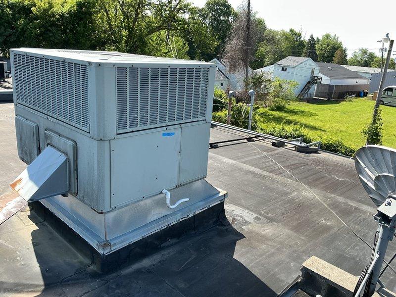 Conducted site assessment of existing rooftop-mounted American Standard packaged air conditioning unit for replacement estimate. Unit is installed on curb adapter on flat membrane roof in commercial application. Customer requested replacement with 2.5 to 3-ton capacity unit, specifying no larger tonnage. Documented existing equipment configuration, roof conditions, refrigerant line routing, and clearances for proper equipment sizing and installation planning.