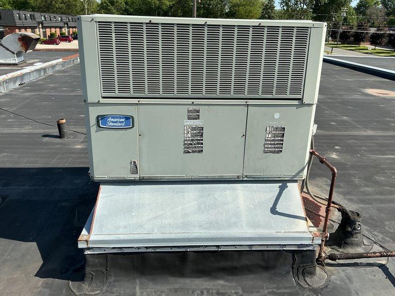 Conducted site assessment of existing rooftop-mounted American Standard packaged air conditioning unit for replacement estimate. Unit is installed on curb adapter on flat membrane roof in commercial application. Customer requested replacement with 2.5 to 3-ton capacity unit, specifying no larger tonnage. Documented existing equipment configuration, roof conditions, refrigerant line routing, and clearances for proper equipment sizing and installation planning.